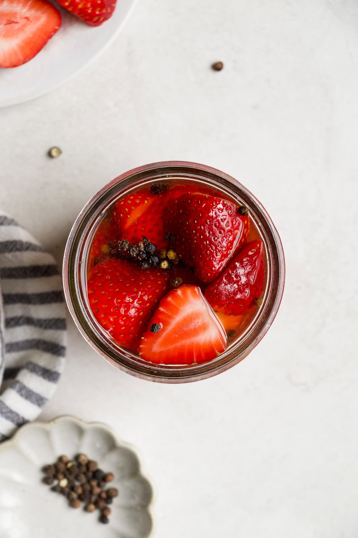 Pickled strawberries in a jar with black peppercorns.