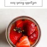 Quick pickled strawberries in a jar with black peppercorns.