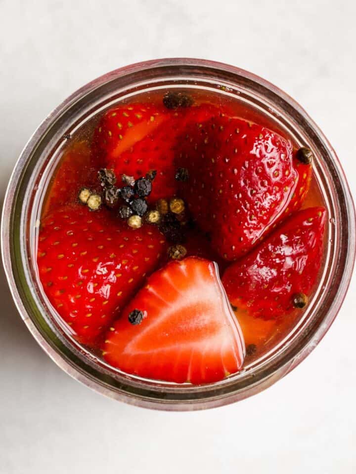 Pickled strawberries in a jar with black peppercorns.