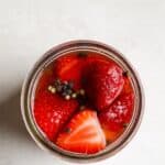 Pickled strawberries in a jar with black peppercorns.