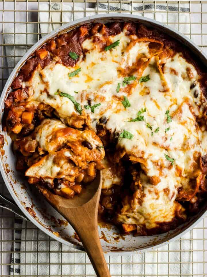 Vegetarian black bean and sweet potato skillet enchiladas being scooped out of pan.