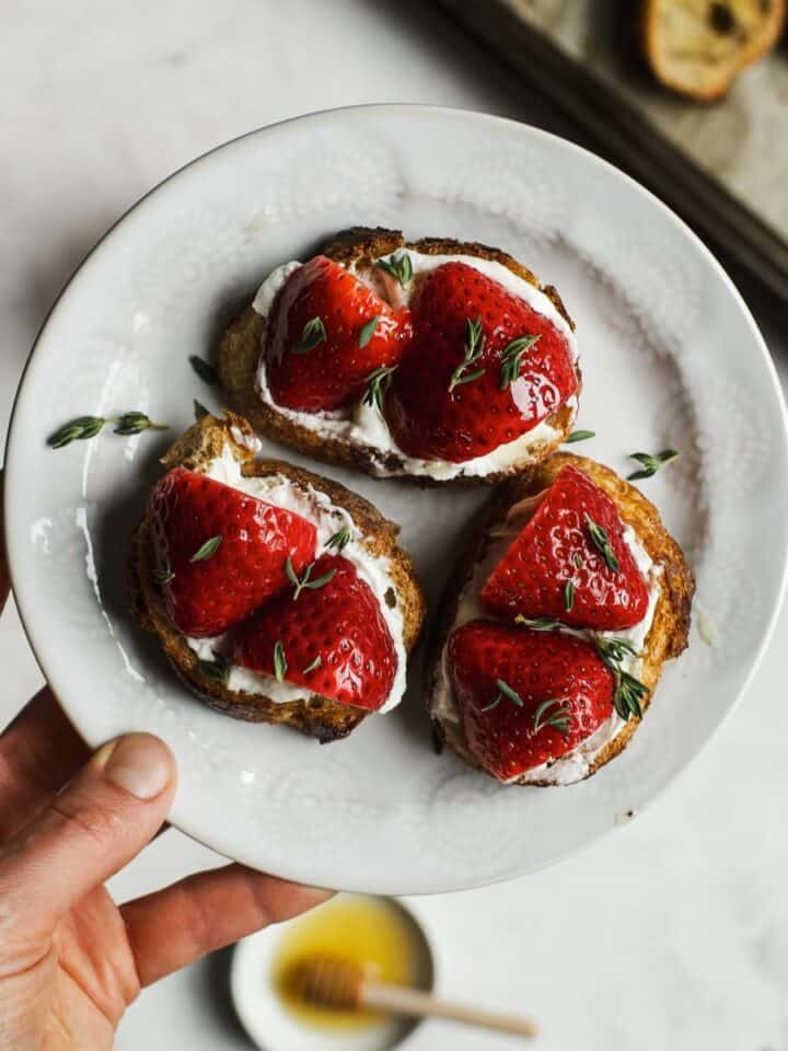 Goat cheese crostini with pickled strawberries on small white plate.