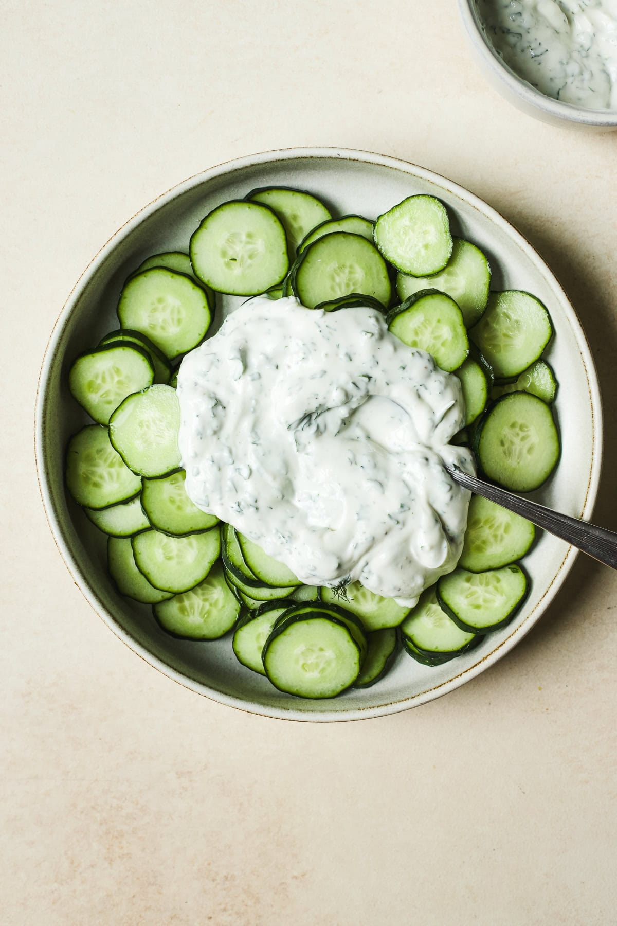 Bowl of cucumber slices topped with lemon herb yogurt sauce.