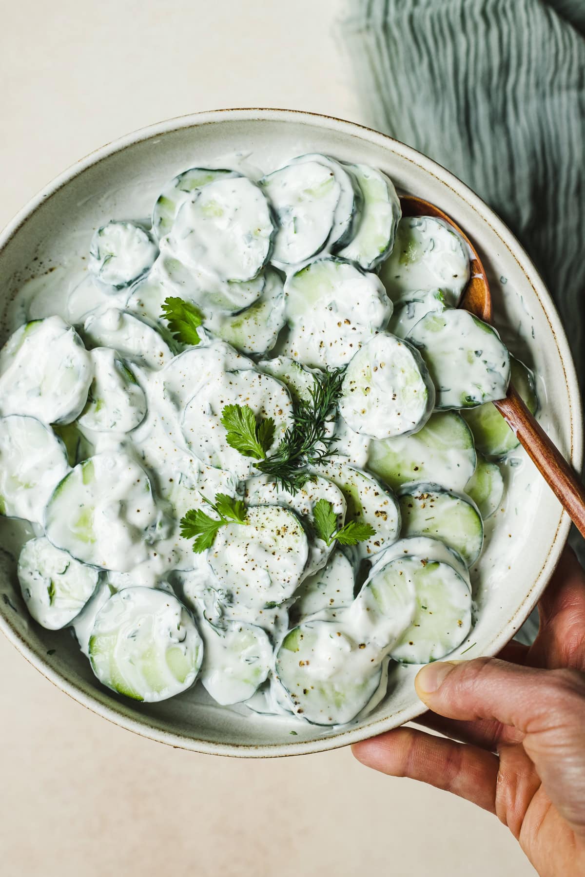 Hand holding creamy cucumber salad in serving bowl.
