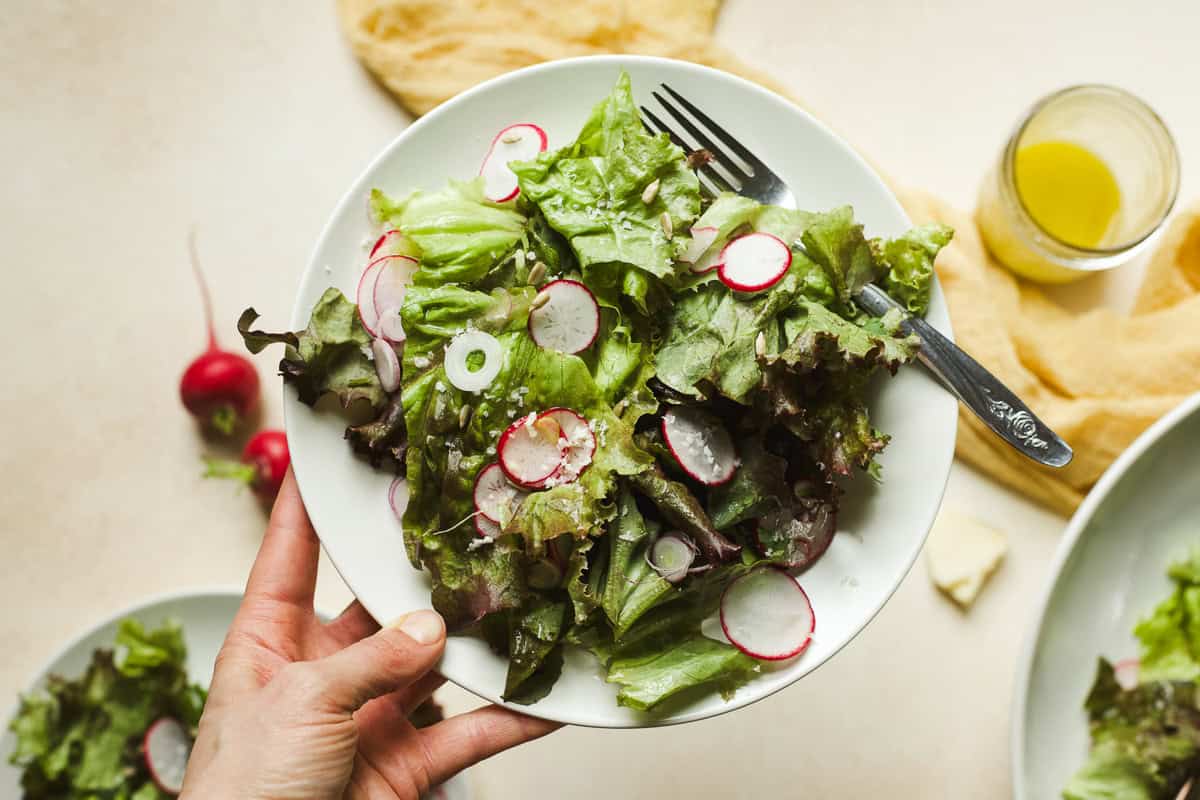 Tera's hand holding a plate of simple green salad.