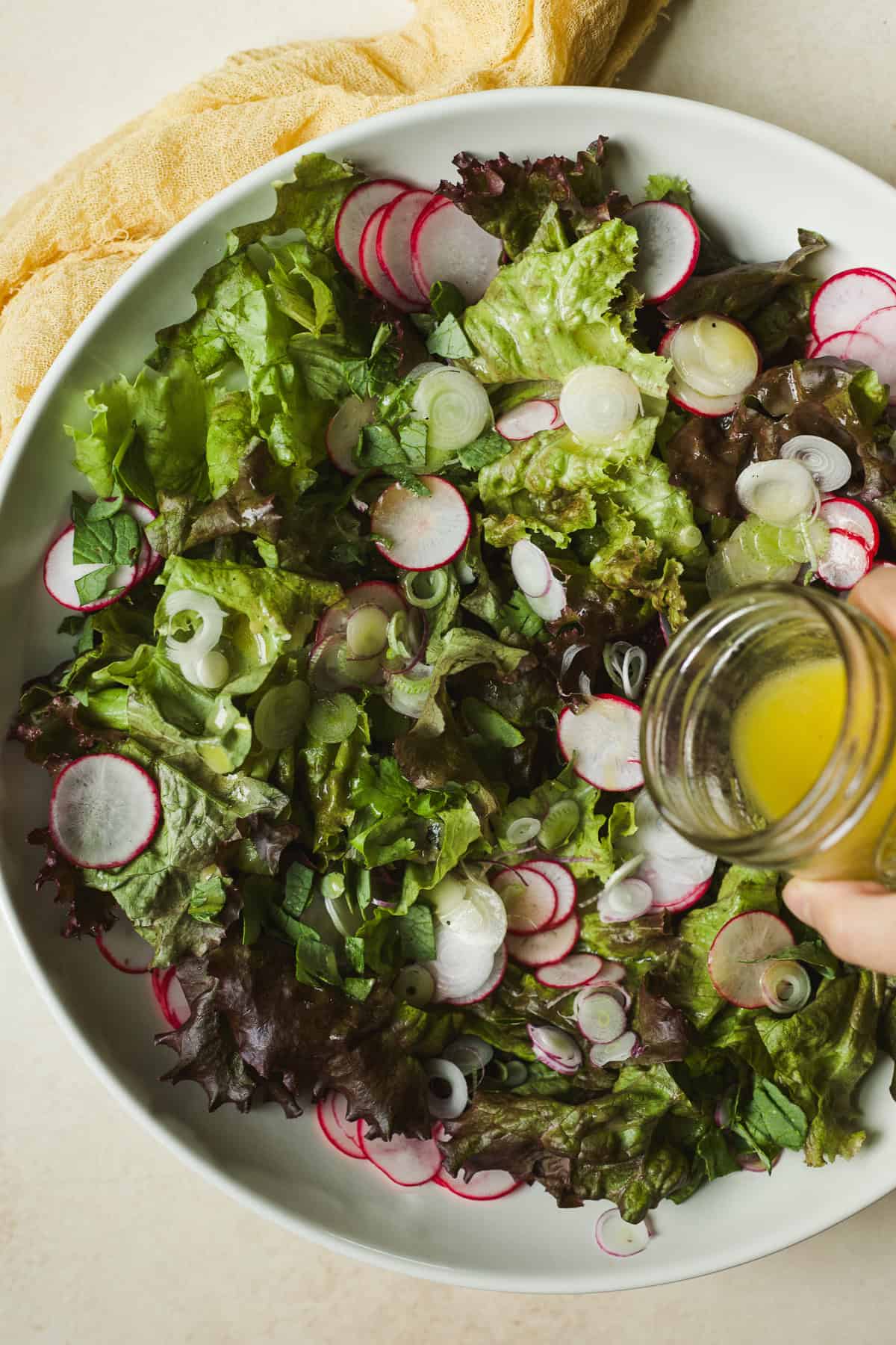 Drizzling lemon vinaigrette over greens in bowl.