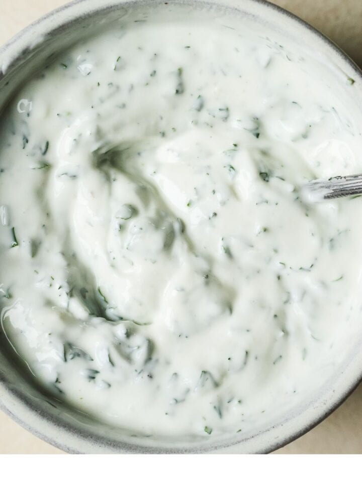 Yogurt sauce with dill, mint, and other herbs mixed together in a bowl.