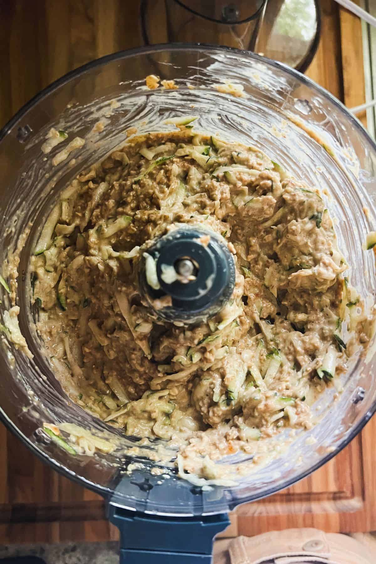 Incorporating shredded zucchini into the zucchini bread batter in a food processor.