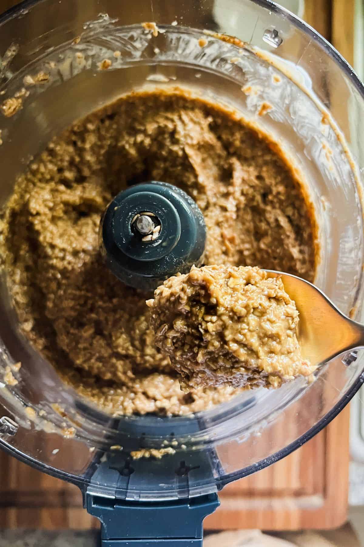 Oat zucchini bread batter in food processor, being scooped up by a spoon.