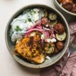 Berbere chicken with dill roasted potatoes in a bowl with creamy cucumber salad and pickled red onions.