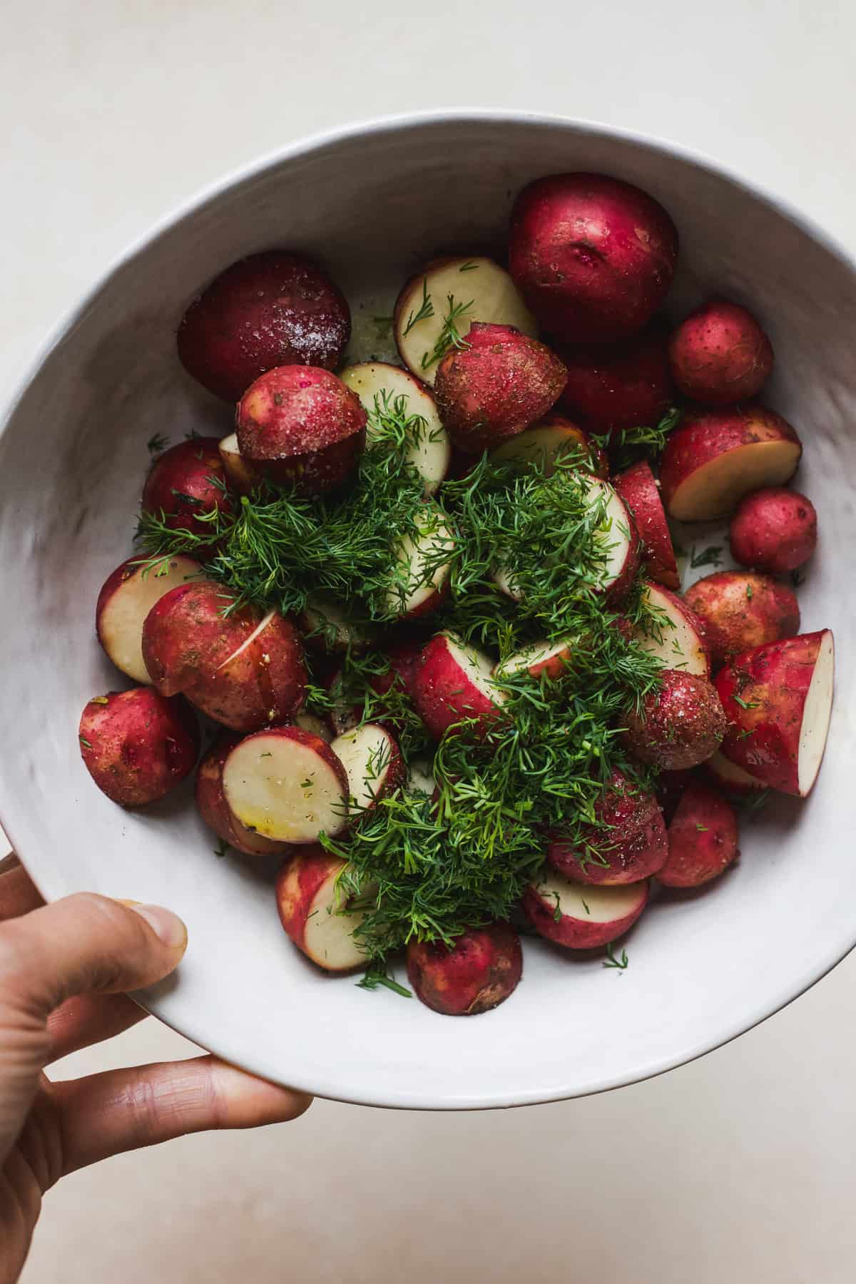 Dill and seasoned potato halves in a bowl.