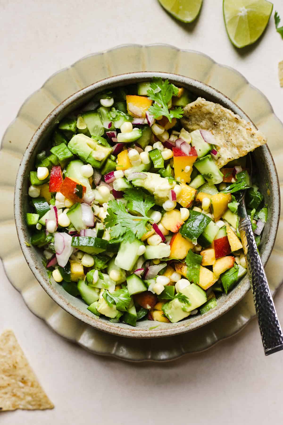 Tortilla chip in a bowl of peach salsa with corn and avocado.