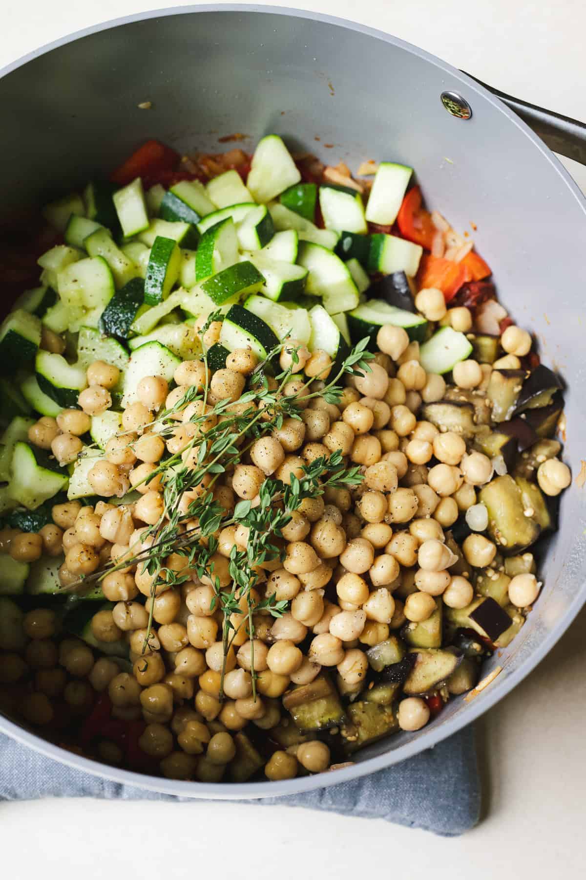 All ratatouille ingredients added to a large pot with chickpeas and fresh thyme.