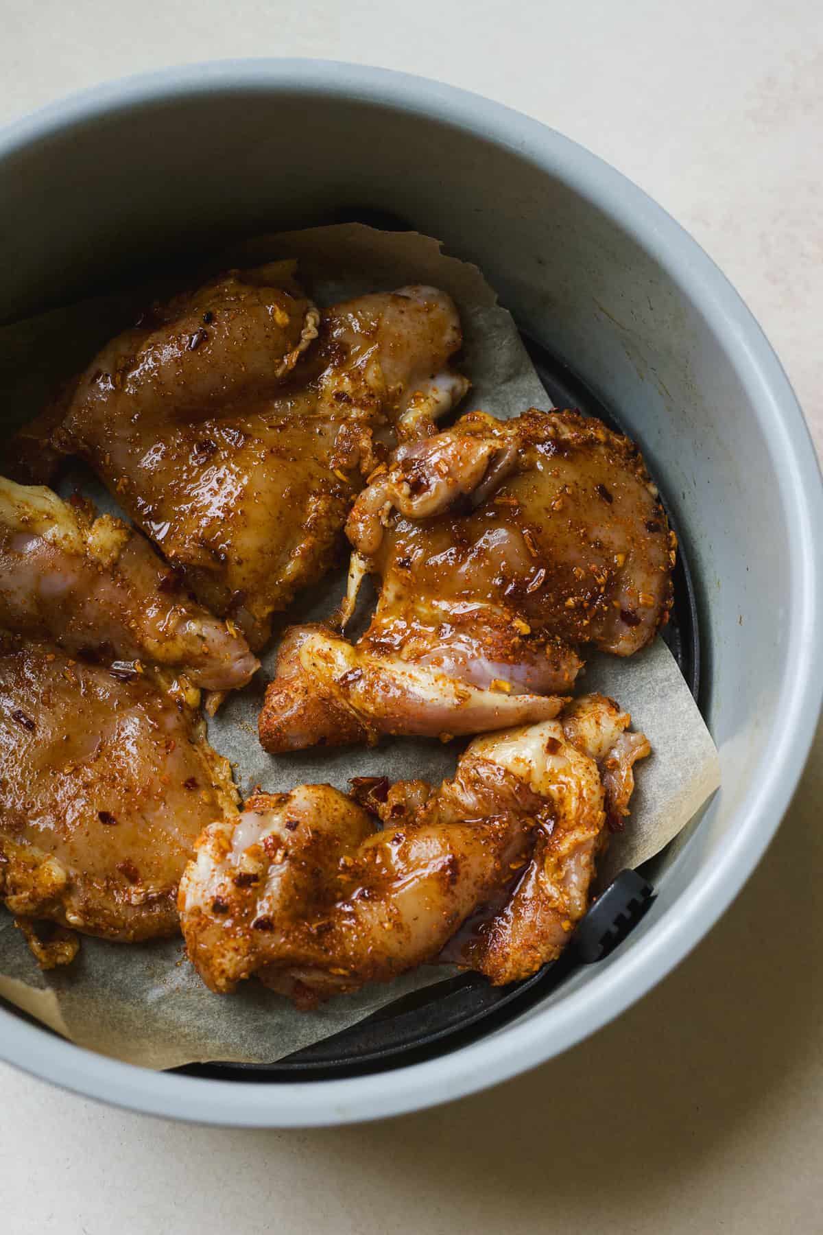 Raw boneless skinless chicken thighs with hot honey and taco spices in air fryer.