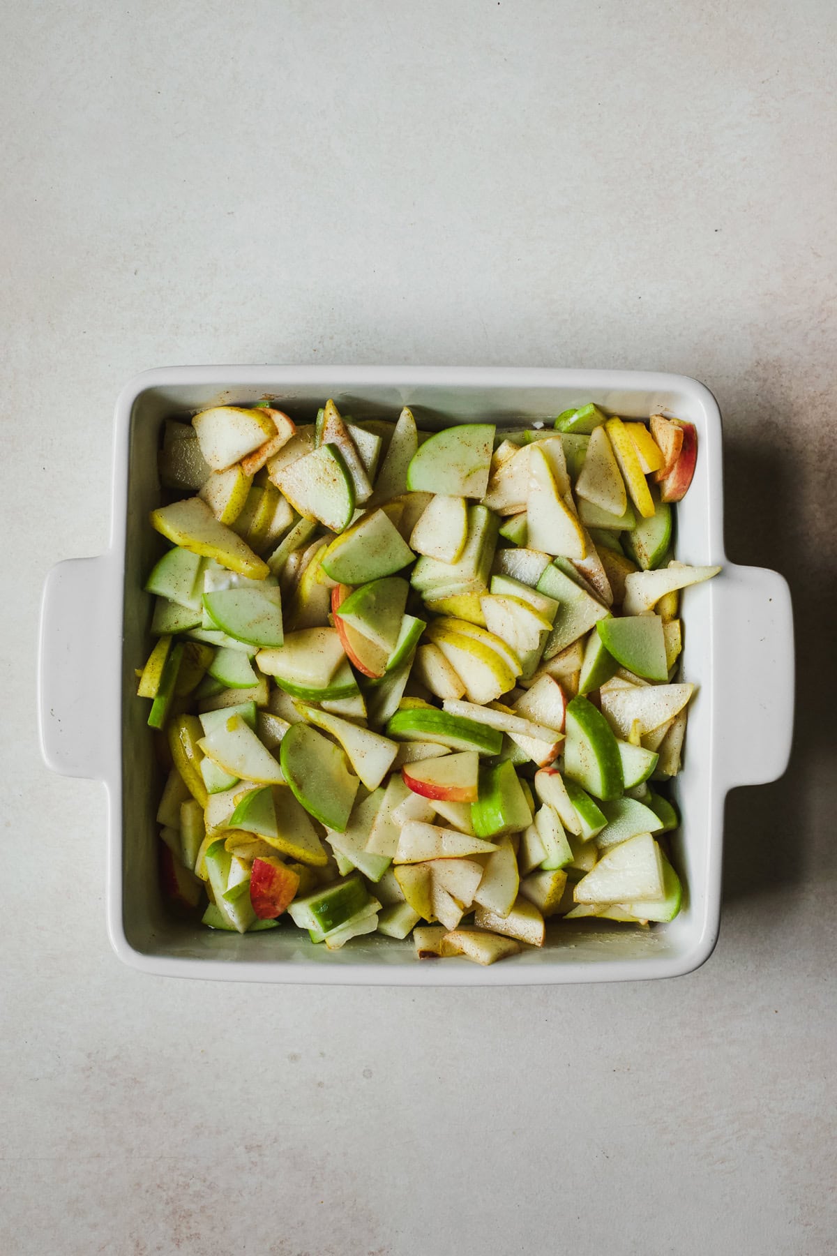 Layering apple pear filling in a baking dish before adding oat topping.