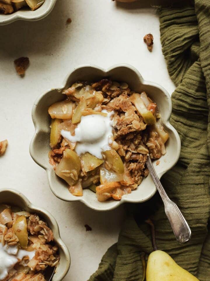 Pear apple crisp in a small bowl, topped with vanilla ice cream.