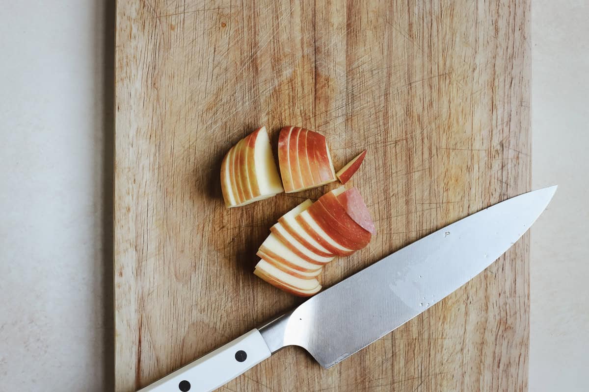 Thinly sliced apples on cutting board with chef's knife.