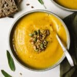 Butternut squash apple soup in a bowl with spoon and toppings.