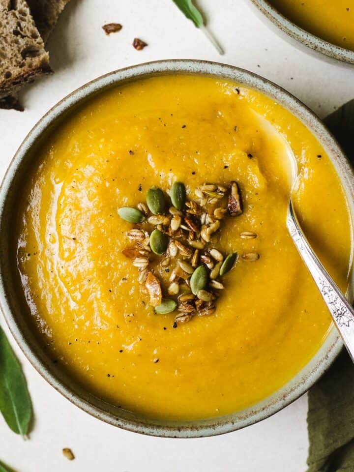 Butternut squash apple soup in a bowl with spoon and toppings.