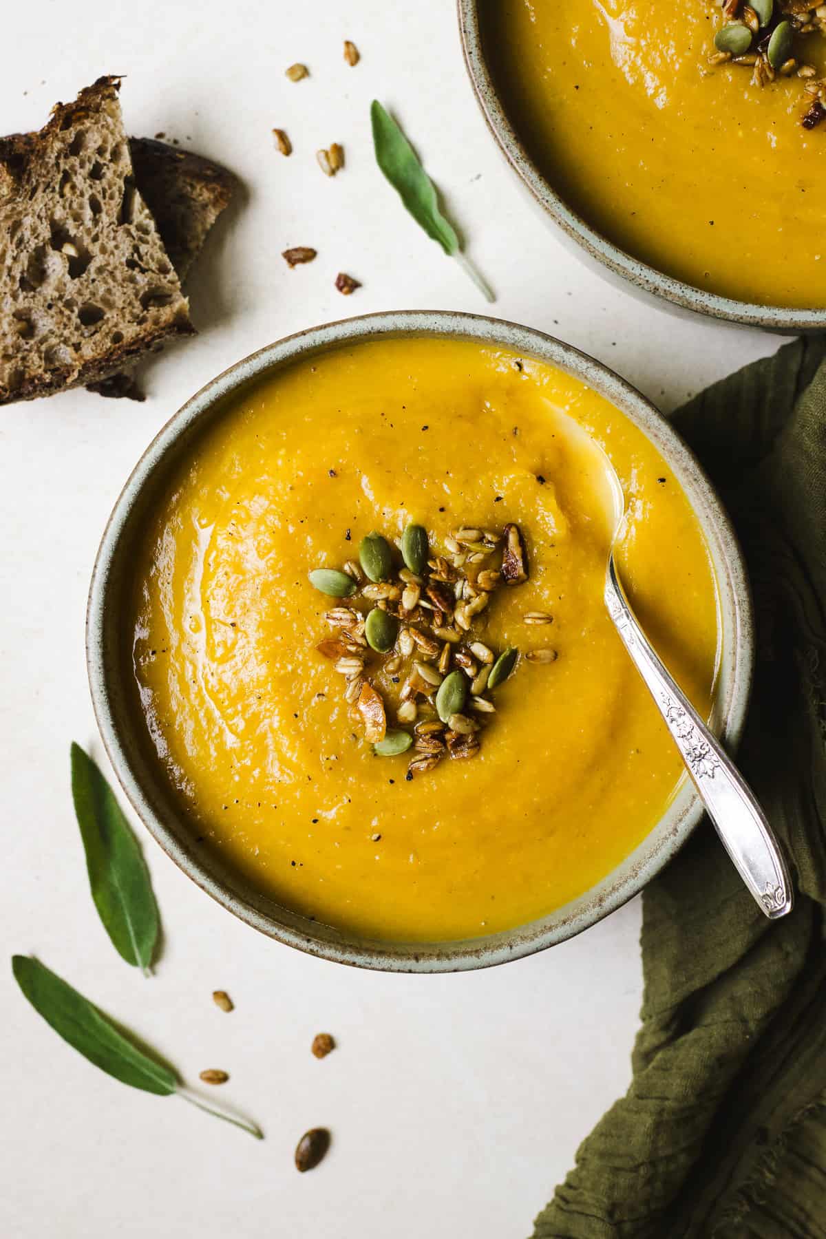Butternut squash apple soup in a bowl with spoon and toppings.