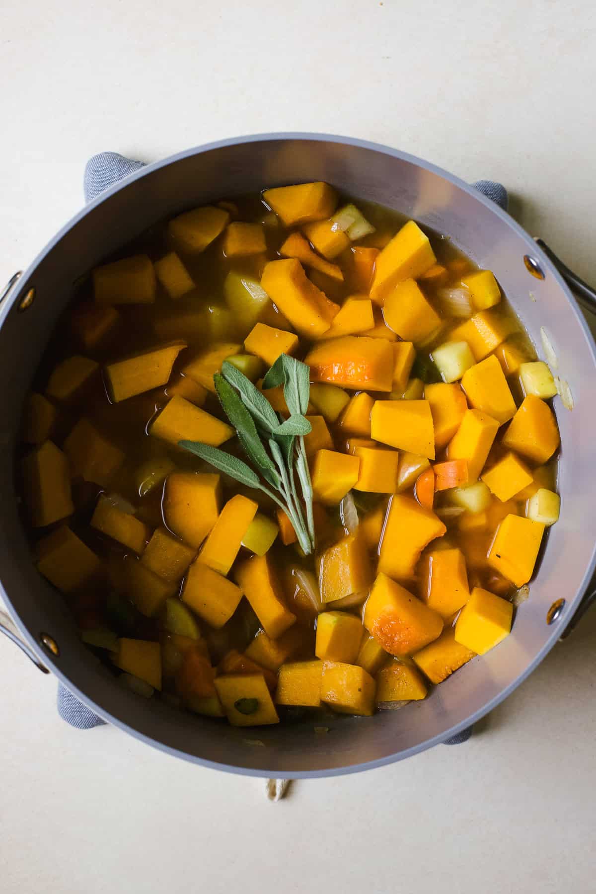 Simmering butternut squash soup with fresh sage in a large pot.