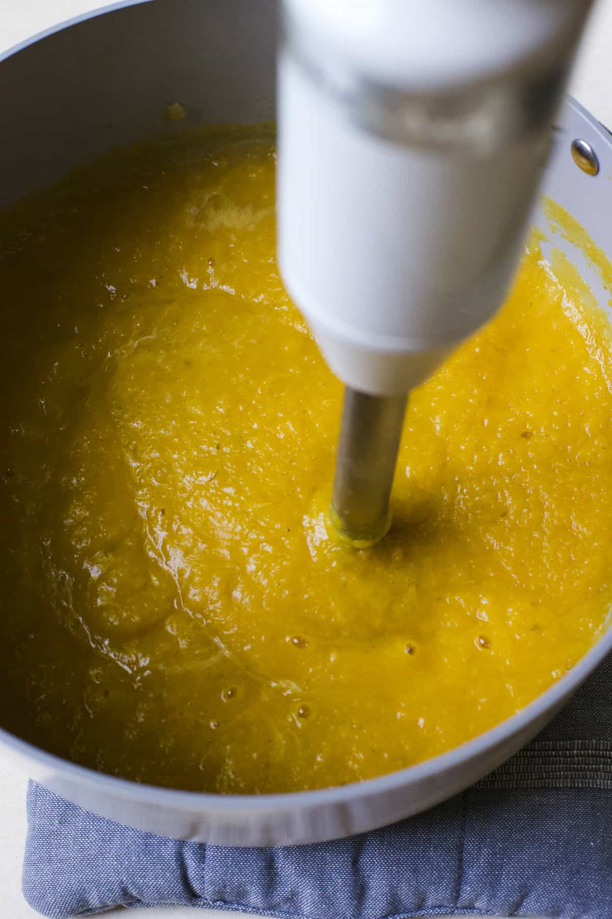 Blending butternut squash and apple soup in a large pot.