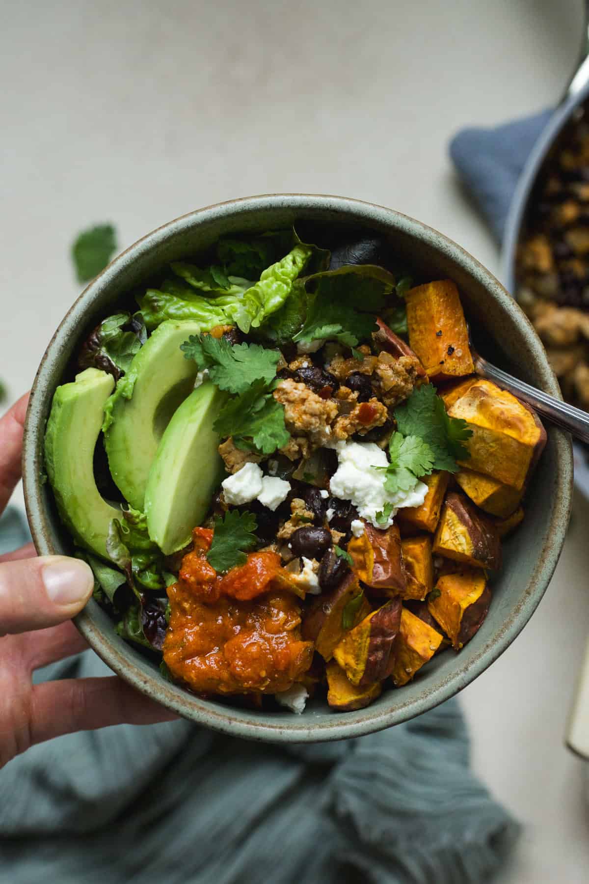 Hand holding a ground chicken taco sweet potato bowl topped with feta, avocado, and cilantro.