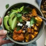 Hand holding a ground chicken taco sweet potato bowl topped with feta, avocado, and cilantro.