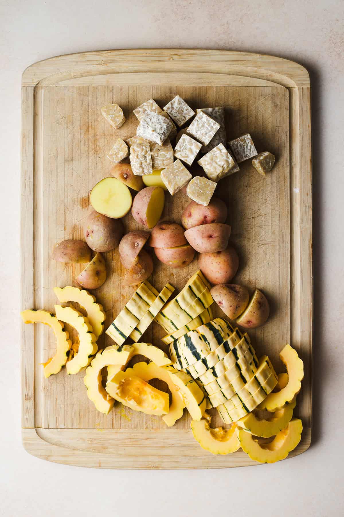 Delicata squash slices, baby red potato halves, and tempeh cubes on a cutting board.