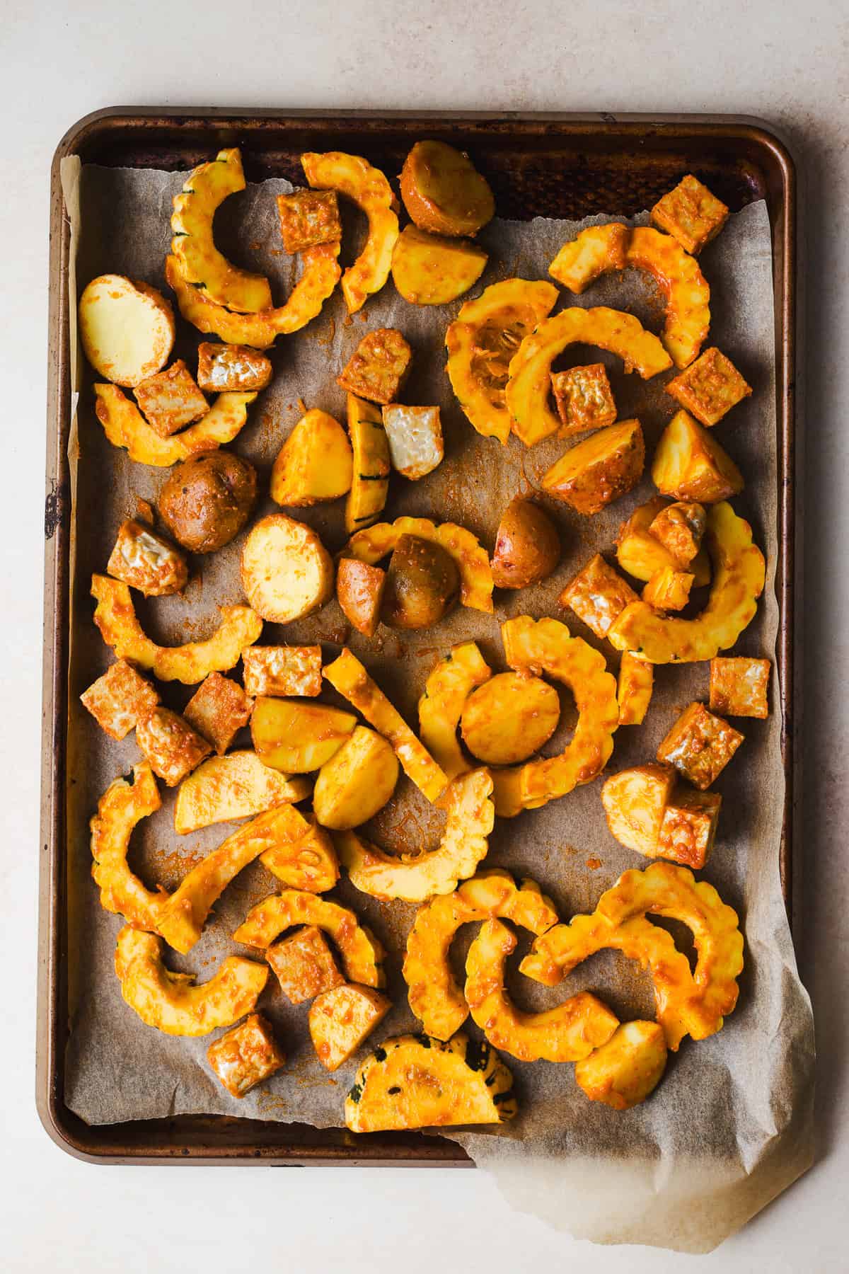 Delicata squash slices, baby red potato halves, and tempeh tossed in miso curry sauce and spread evenly on sheet pan.
