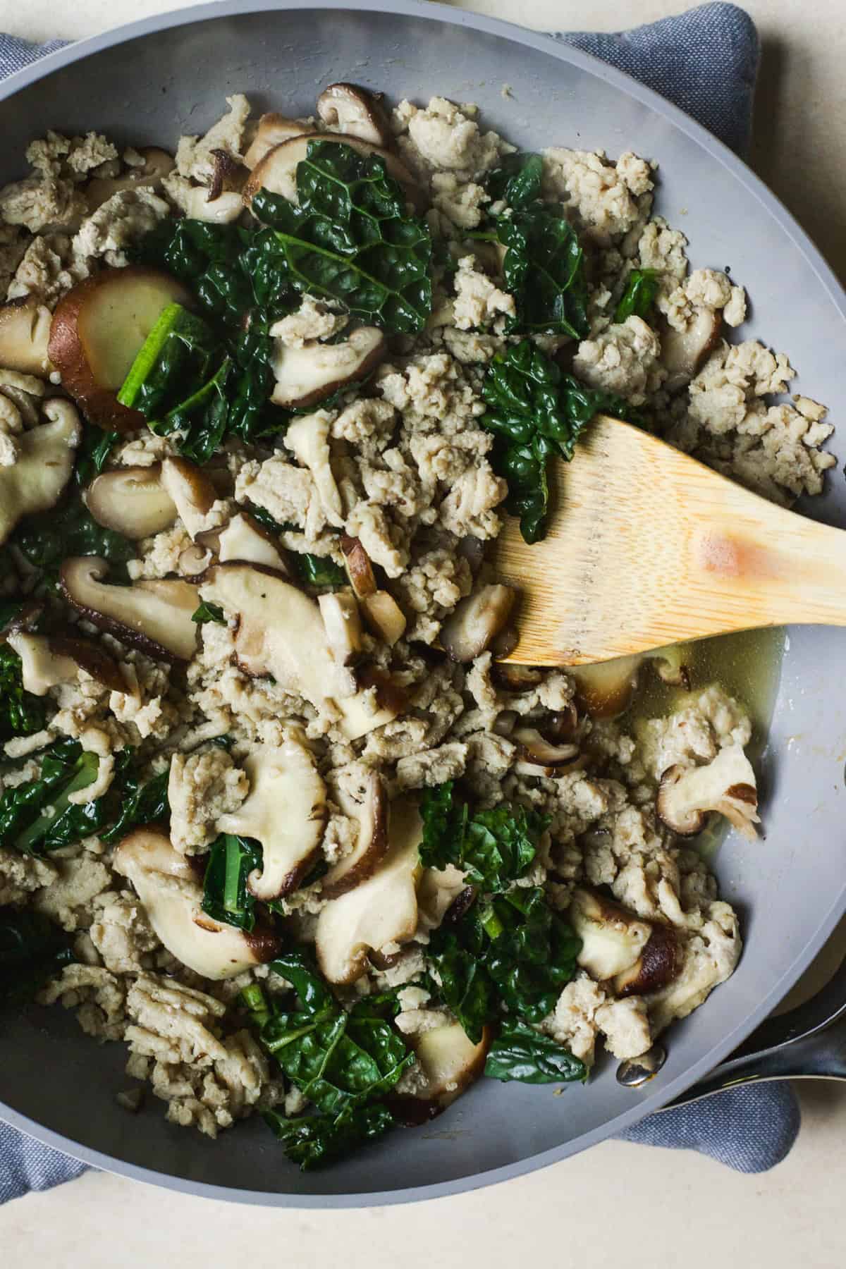 Browned ground chicken with shiitake mushrooms and kale in a skillet.