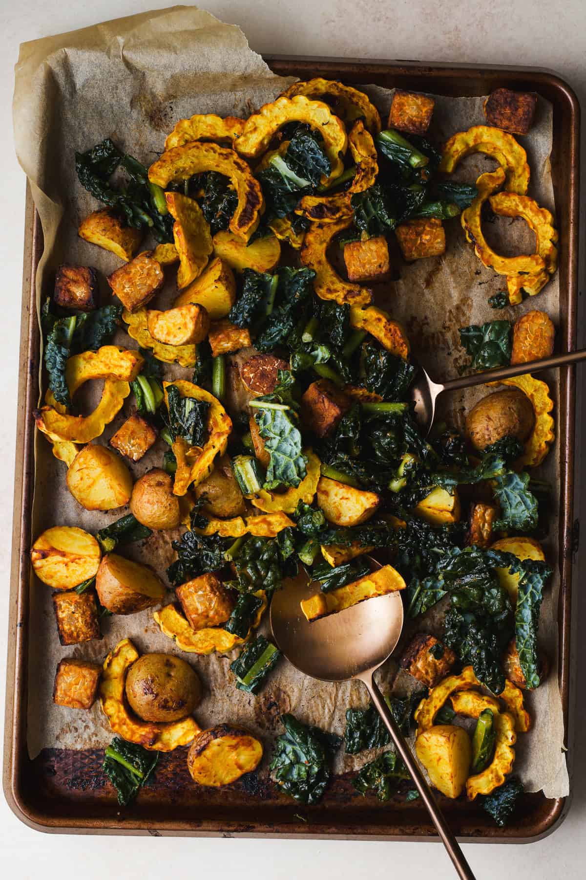 Miso curry delicata squash with potatoes, tempeh, and kale tossed together on a sheet pan.