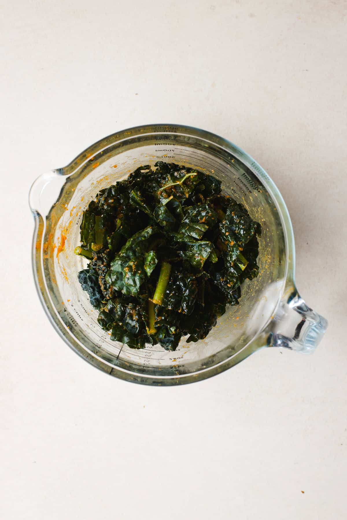 Chopped kale massaged in miso curry sauce, in large glass measuring cup.