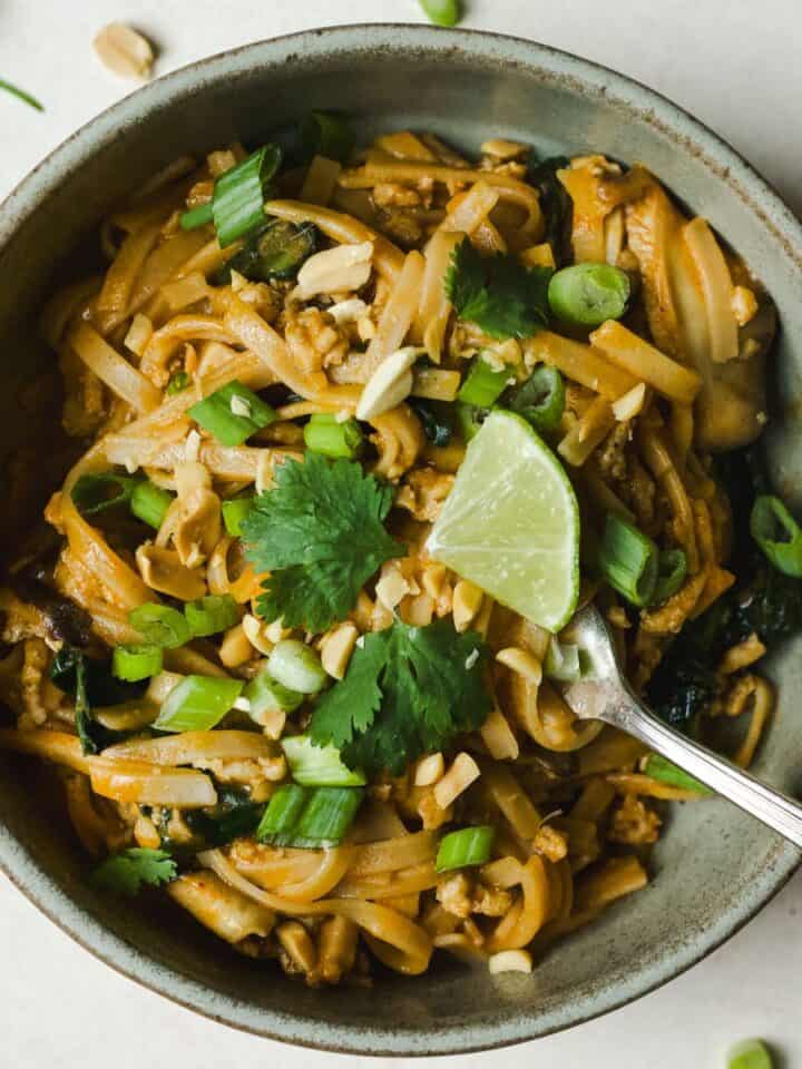 Thai curry noodles with chicken in a bowl with lime and cilantro.