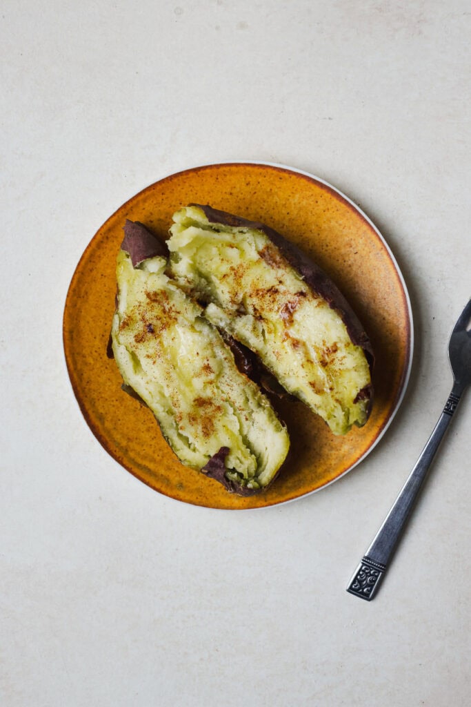 A baked Japanese purple sweet potato with butter and cinnamon on a small plate with a fork.