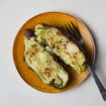 A baked Japanese purple sweet potato with butter and cinnamon on a small plate with a fork.
