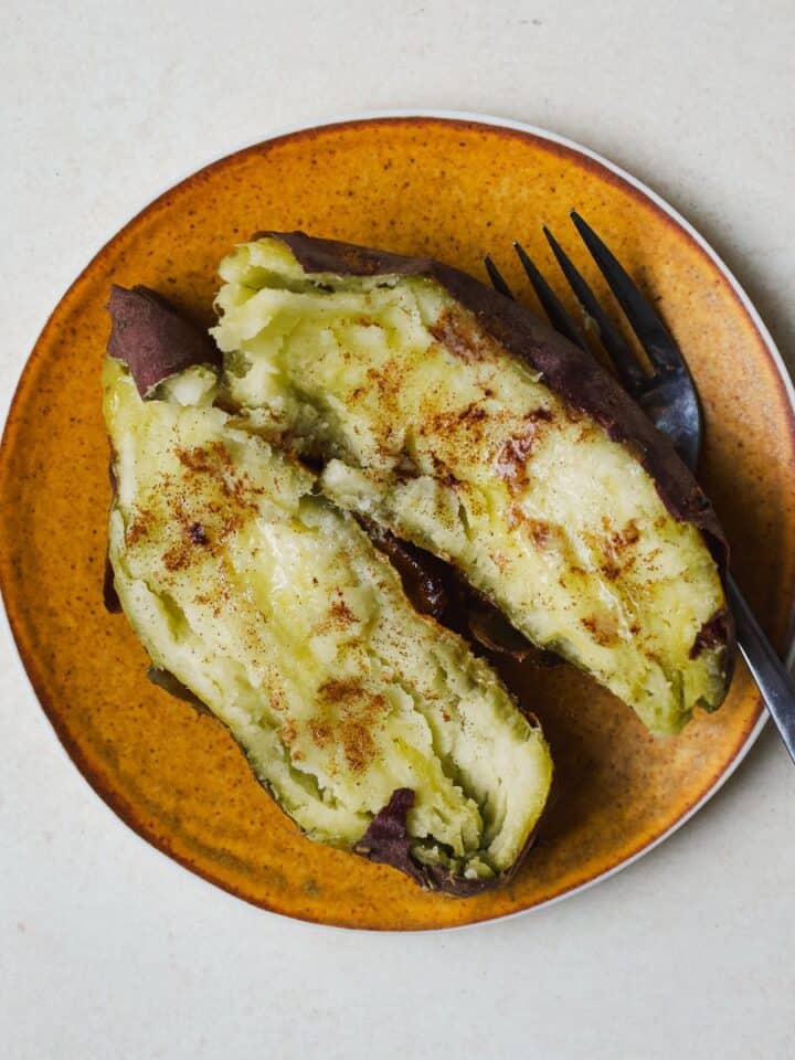 A baked Japanese purple sweet potato with butter and cinnamon on a small plate with a fork.