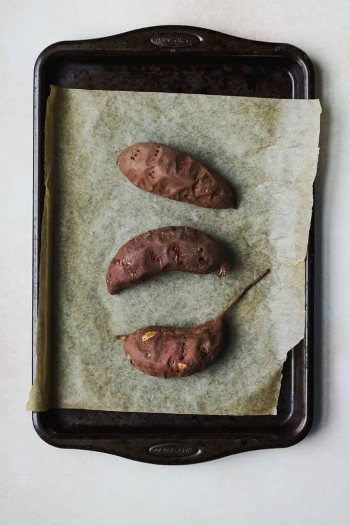 Three baked Murasaki sweet potatoes on a sheet pan.