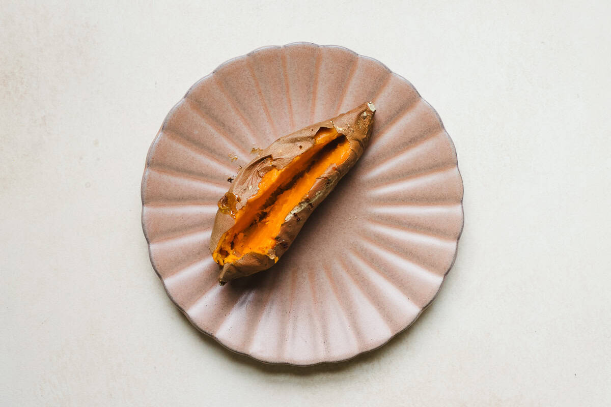A baked sweet potato split open to be stuffed with black beans, on a plate.