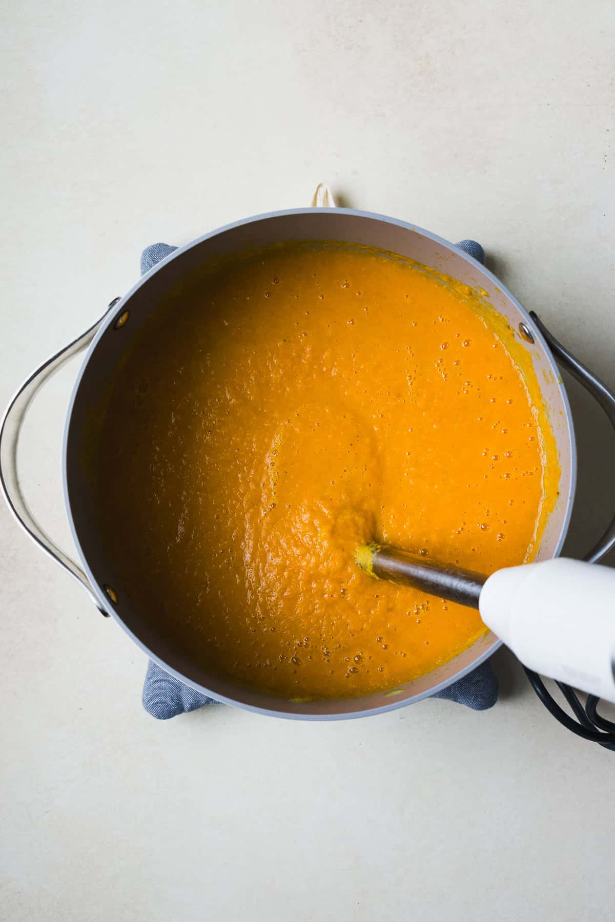 Using an immersion blender to blend the carrot sweet potato soup in a dutch oven.