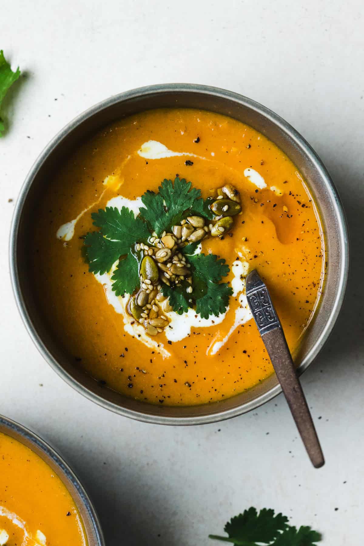 Bowl of spiced carrot and sweet potato soup with a creamy swirl on top, with cilantro and seeds.