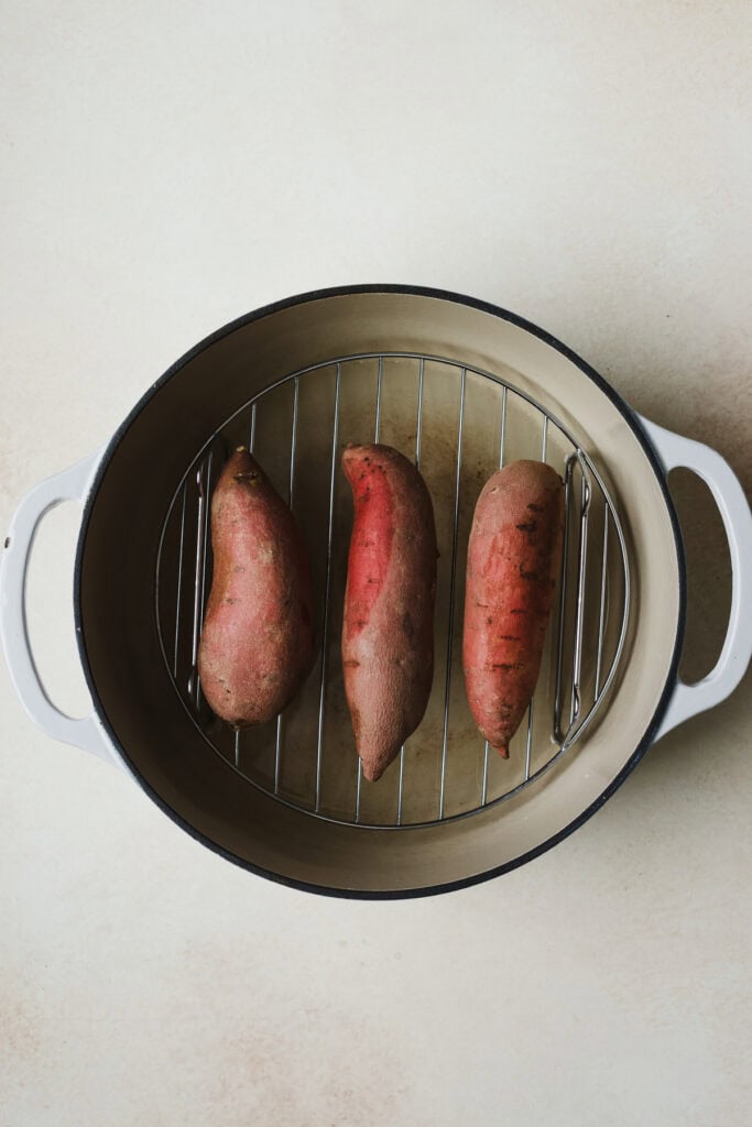 Three Japanese purple sweet potatoes on a steaming rack in a dutch oven.
