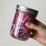 Hand shaking a jar to mix pickled red onion ingredients.