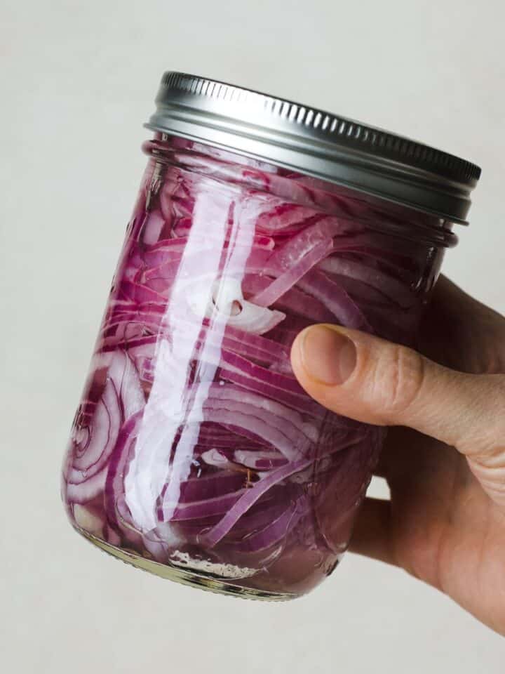 Hand shaking a jar to mix pickled red onion ingredients.