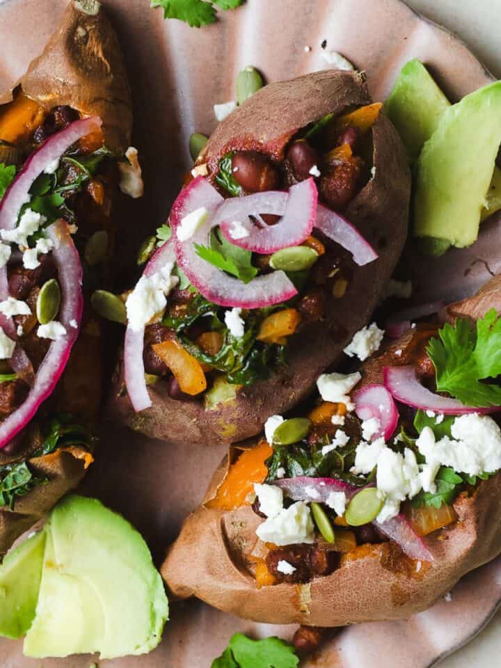Three smoky black bean stuffed sweet potatoes with toppings on a plate.