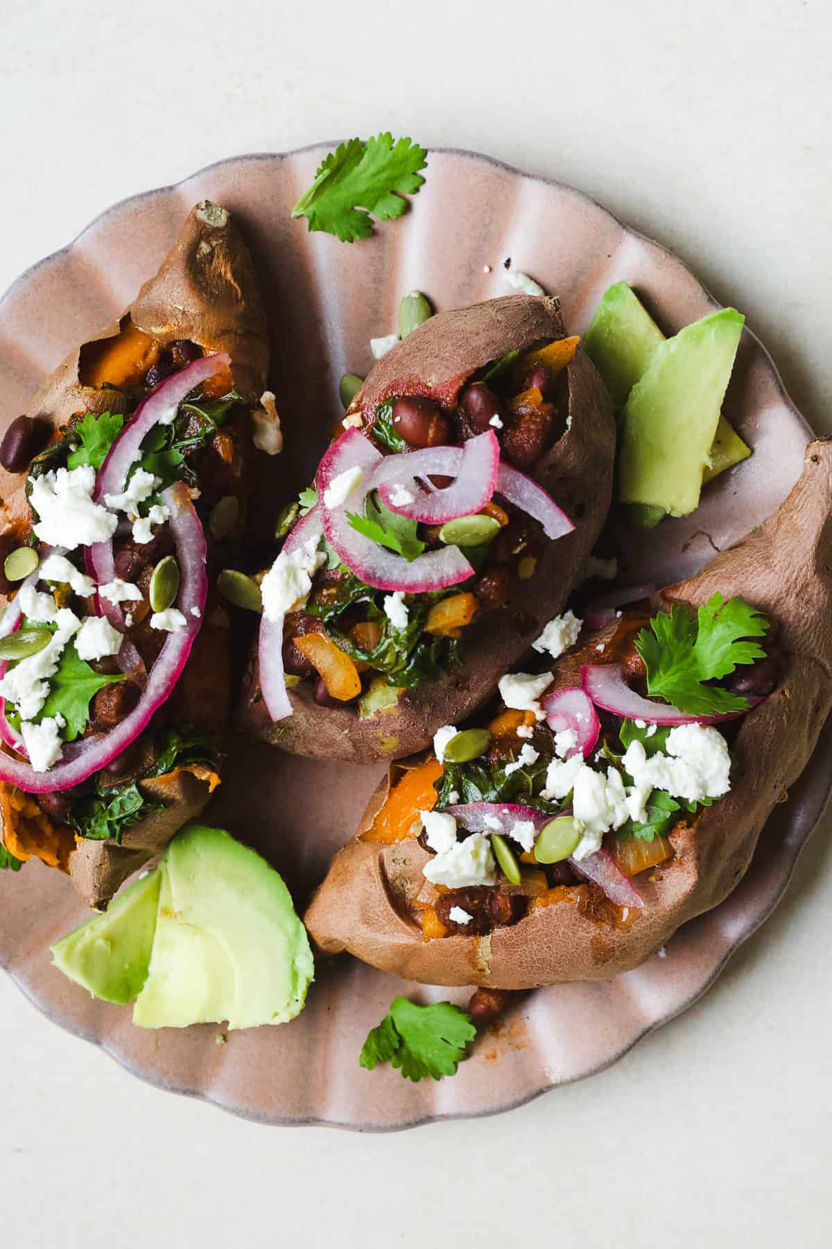 Three smoky black bean stuffed sweet potatoes with toppings on a plate.