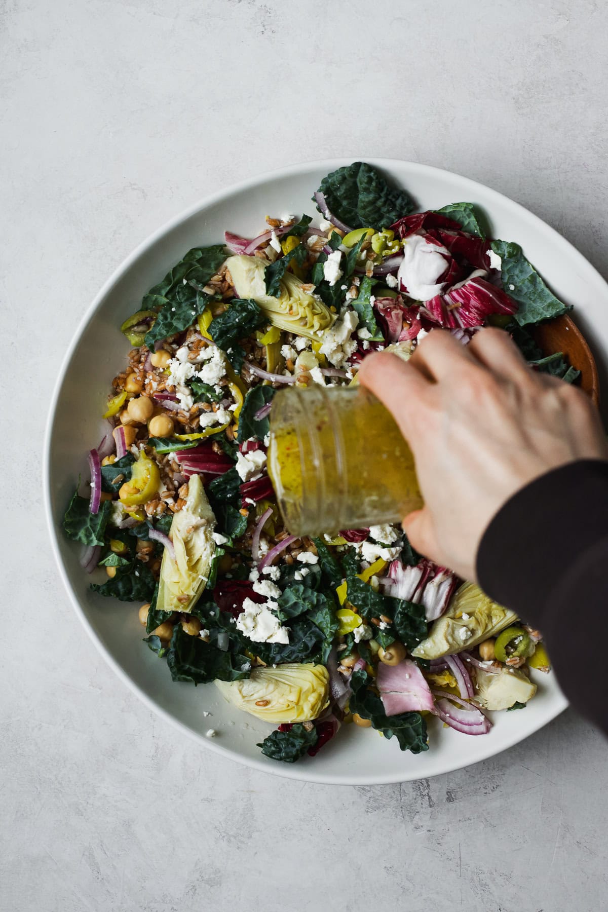 Pouring peperoncini brine Italian vinaigrette over farro salad.
