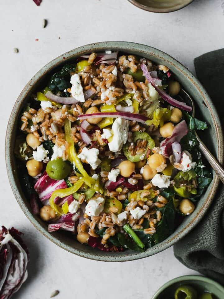 Bold and briny kale farro salad with chickpeas in a bowl with a fork.