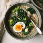 A bowl of savory steel cut oatmeal topped with sautéed kale, a jammy egg, and chili crisp.
