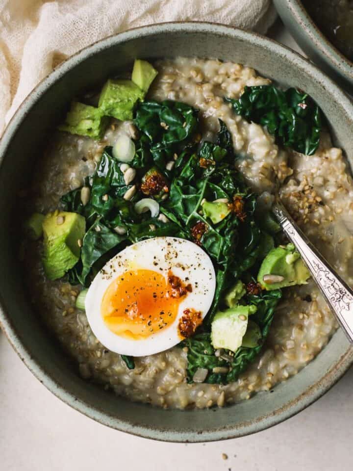 A bowl of savory steel cut oatmeal topped with sautéed kale, a jammy egg, and chili crisp.